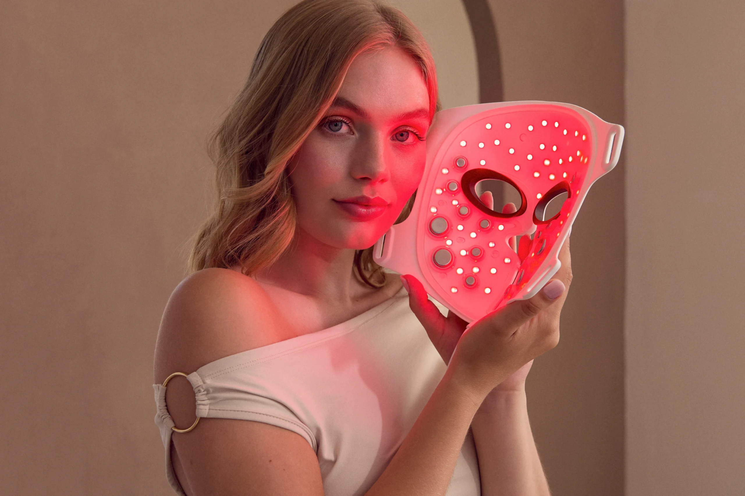 Uśmiechnięta kobieta siedząca na kanapie i trzymająca maskę LED z EMS do domowego liftingu twarzy i likwidacji chomików